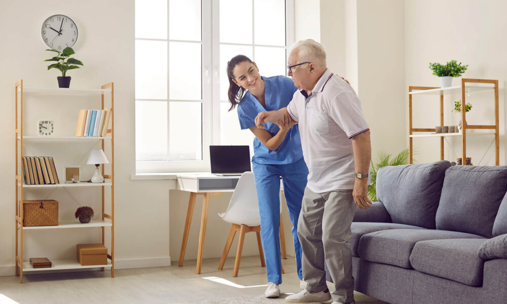 a female registered NDIS nurse helping an elderly man to standup