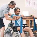 Smiling friendly in-home male nurse in uniform supporting an old man with a walking stick