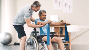 Smiling friendly in-home male nurse in uniform supporting an old man with a walking stick